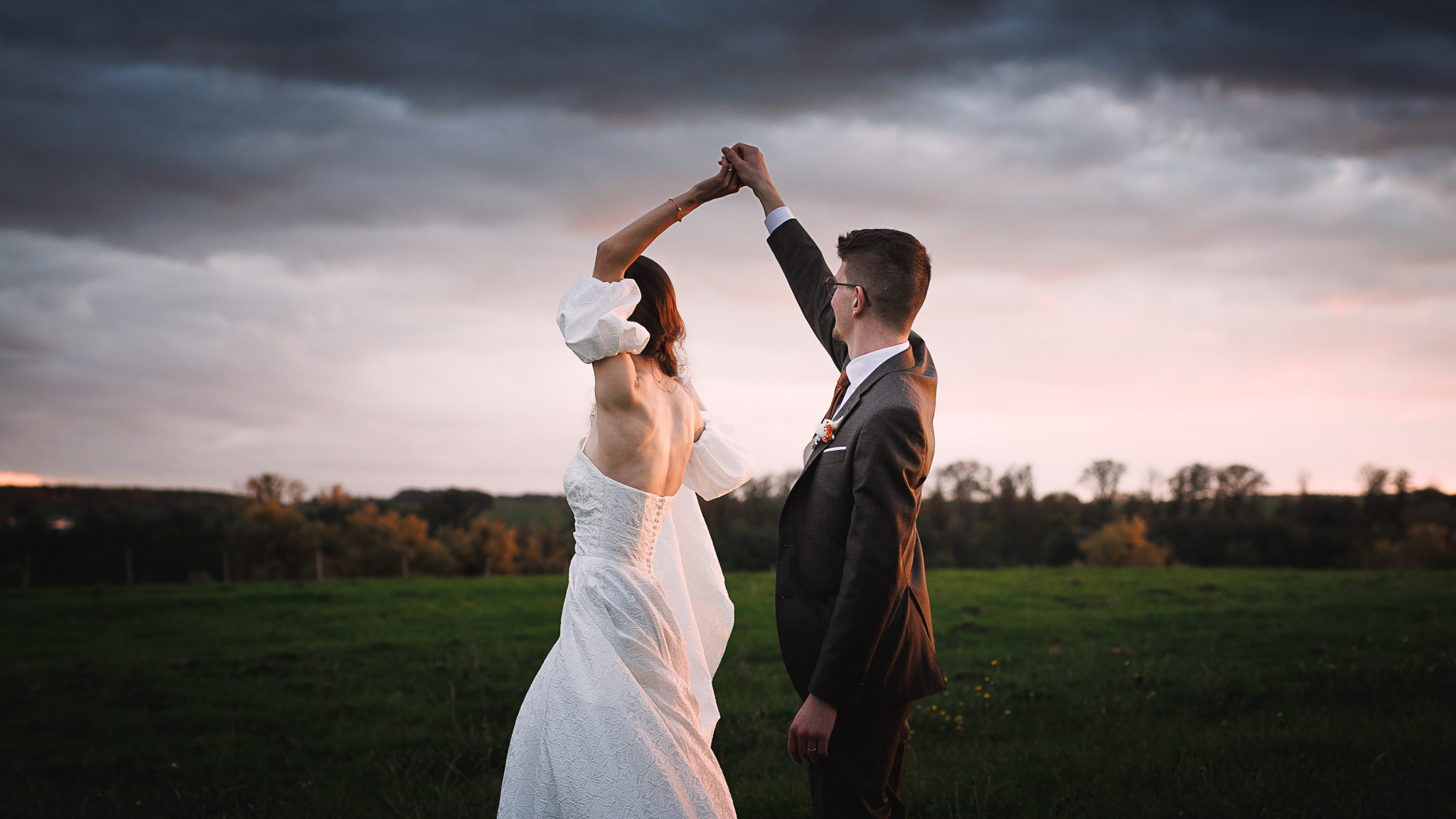 Une mariée dans dans un pré, la main tenue au dessus d'elle par son époux